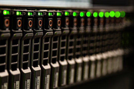 Closeup of server rack with multiple hard drives in data center. Green LED indicators show active status. Technology and infrastructure for data storage and cloud computing.