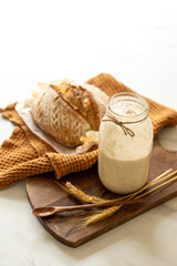 Crispy sourdough bread sits beside a glass jar filled with active starter, accompanied by a rustic...