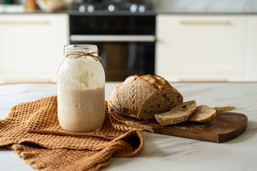 Crispy sourdough bread sits beside a glass jar filled with active starter, accompanied by a rustic...