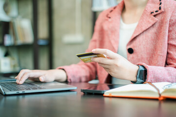 A person in a pink blazer using a laptop and holding a credit card, representing online shopping...