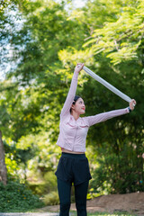 A woman in sportswear stretches in a park surrounded by vibrant greenery, enjoying a sunny day...