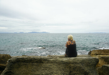 A woman sitting on a rock around Waipu pancake rocks in Waipu, New Zealand.