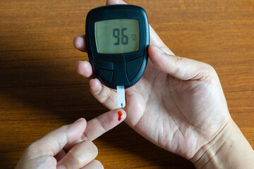 Woman's hands checking diabetes and hyperglycemia with digital blood sugar meter. Healthcare and...