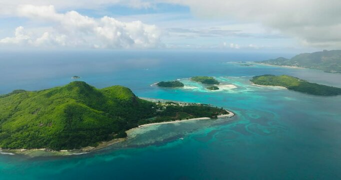 Island with green vegetation, vibrant turquoise waters, and coral reefs under a clear sky. Seychelles, Mahe. Ile au cerf island.