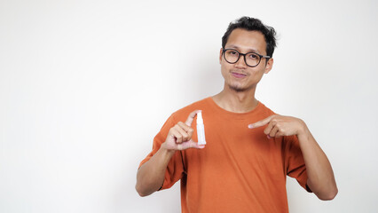 A man in an orange shirt is holding a bottle of medicine and pointing to it