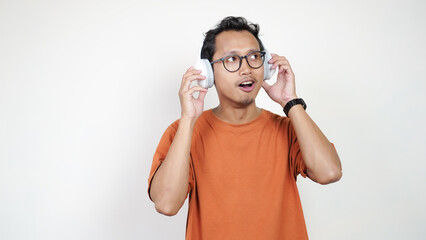 A man in an orange shirt is wearing headphones and talking on a cell phone