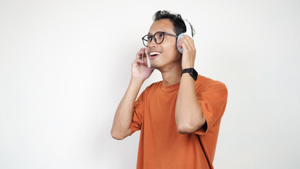 A man in an orange shirt is wearing headphones and talking on a cell phone