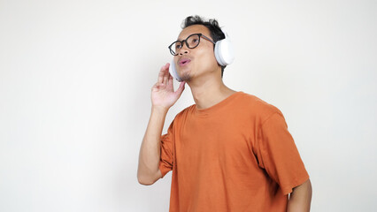 A man in an orange shirt is wearing headphones and talking on a cell phone
