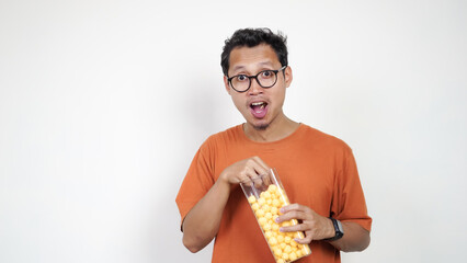 A man in an orange shirt is holding a jar of yellow candies