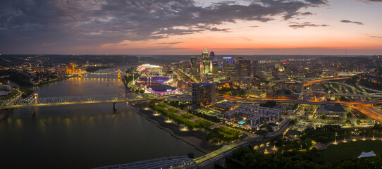 Fototapeta premium Cincinnati city, Ohio, USA with bridge highway traffic driving cars in downtown district. American city skyline with brightly illuminated high commercial buildings at night