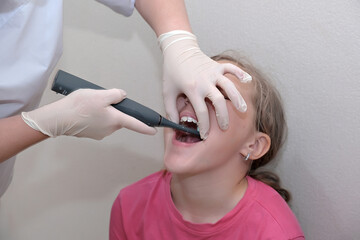 A small child gets his teeth cleaned at home. The child is sitting in a pink shirt, and the dentist...