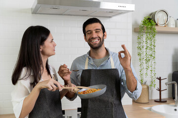 Couple enjoying cooking together at home, man smiling and making okay gesture while tasting delicious food