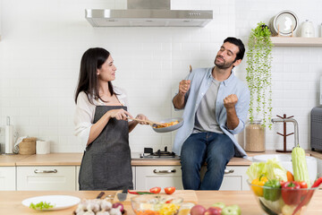 Man reacts with excitement after tasting food while woman holds pan, happy couple cooking together in kitchen