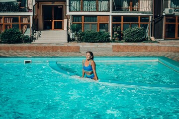 A woman is in the water, smiling and enjoying herself. The water is blue and the pool is surrounded by a white ledge.