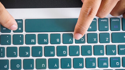 Top view of finger pressing command and C or cmd + C shortcut keys for copy on a green wireless...