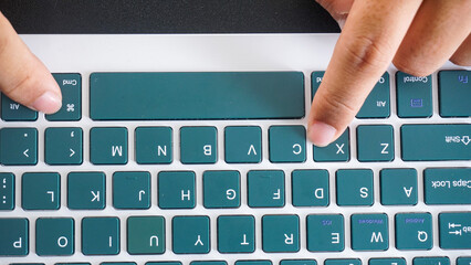 Top view of finger pressing command and X or cmd + X shortcut keys for cut on a green wireless...