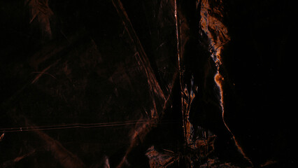 Distressed foil. Rust texture. Orange dark color light flare dust scratches surface on black uneven wrinkled abstract background.