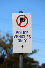 Police Vehicles Only parking sign mounted on a metal pole with a tree and blue sky in the background