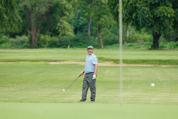 Fototapeta premium Elderly Asian man enjoying the morning round of golf in soft and warm sunlight.