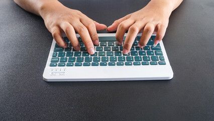 A man typing on a green modern wireless computer keyboard isolated on black background