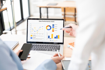 Rear view. Two Young businesswoman is sitting at table, working on laptop with graphs, charts, diagrams, schedules on screen