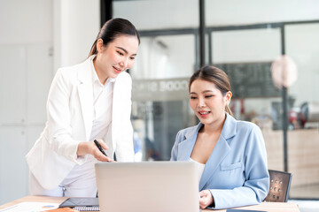 Two young asian businesswomen discussing work over laptop in office