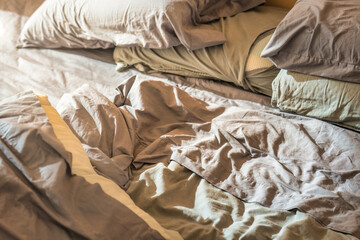 Sunlight streams into a room, illuminating a messy unmade bed with wrinkled sheets and disheveled pillows