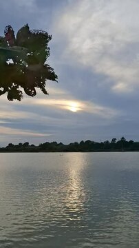 Beautiful sunset over a calm lake with a gentle breeze swaying tree leaves, creating a peaceful and serene landscape