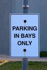 Parking In Bays Only sign mounted on a metal pole with green grass in the background