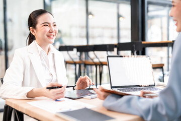 Two young asian businesswomen discussing work over laptop in office