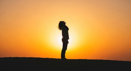 Silhouette of a person standing against a vibrant sunset on a hilltop