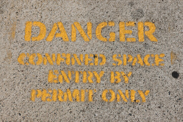 Danger - Confined Space - Entry By Permit Only sign painted in yellow on a concrete surface