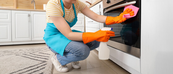 Female janitor cleaning oven in kitchen