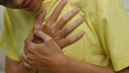 Asian man holding chest in pain.