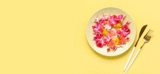 Plate with different beautiful edible flowers and cutlery on yellow background