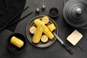 Plate and bowl with boiled corn cobs on black background