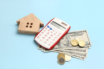 Wooden house, money and calculator on blue background