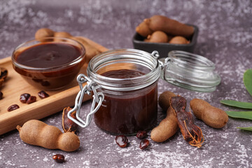 Jar and bowl of tasty tamarind jam with fruits on grey background