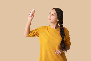Beautiful young Asian woman with mosquito repellent spray on beige background