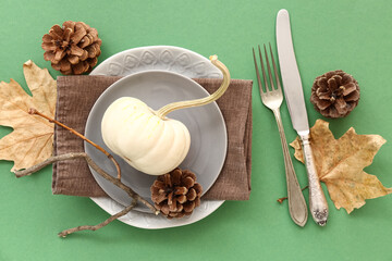 Autumn table setting with pumpkin, cones and dried leaves on green background