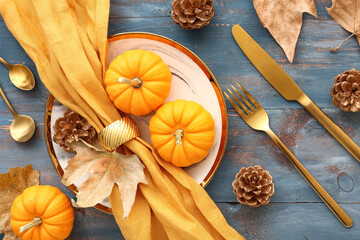 Autumn table setting with pumpkins, cones and dried leaves on blue wooden background