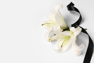 Beautiful lily flowers with black funeral ribbon on white background