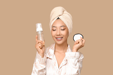 Young Asian woman with reusable cotton pad and cleanser on brown background