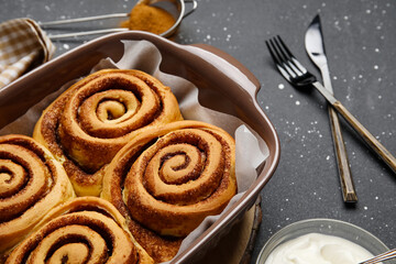 Baking dish with tasty cinnamon rolls on black background