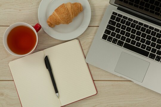 Fototapeta Laptop, lemon tea, croissant and diary on table