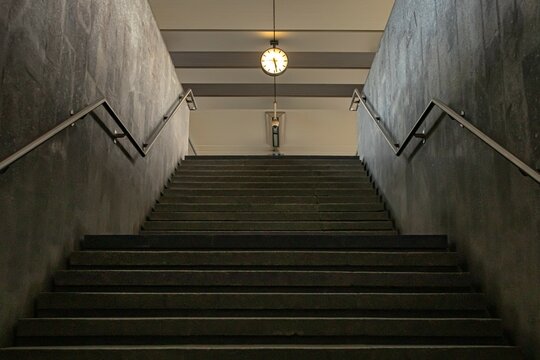Modern indoor staircase with a clock above, symmetrical architecture in a public station. Empty steps, clean lines, travel and urban design concept