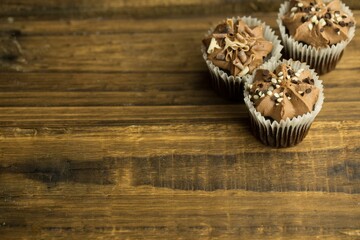 Three chocolate cupcakes are being shown in flat design on wooden tabletop, copy space