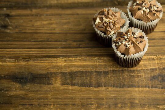 Naklejki Three chocolate cupcakes are being shown in flat design on wooden tabletop, copy space