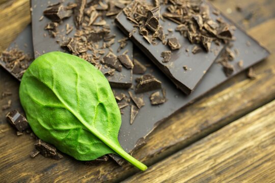 Fototapeta Flat design showing spinach leaf lying diagonally on dark chocolate and pieces, shavings on wood