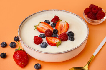 Bowl of tasty semolina porridge with fresh berries on orange background